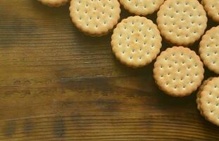 A round sandwich cookie with coconut filling lies in large quantities on a brown wooden surface. Photo of edible treats on a wooden background with copy space