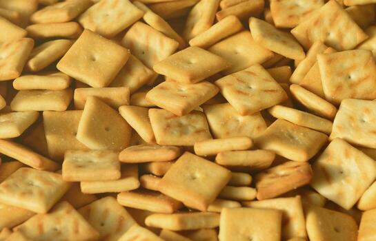 A lot of small cookies are square shaped. A pattern of a yellow salt cracker. Background image with salted pastry photo