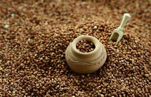Background image of a large pile of buckwheat, in the middle of which lies a small jug and a wooden spatula for cereals photo