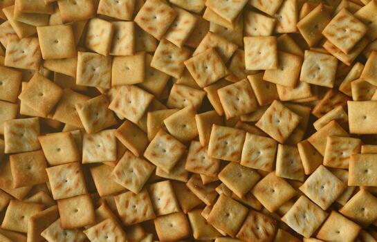 A lot of small cookies are square shaped. A pattern of a yellow salt cracker. Background image with salted pastry photo