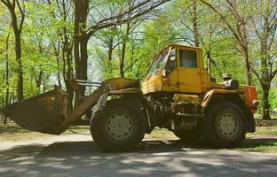 The city improvement team removes the fallen leaves in the park with an excavator and a truck. Regular seasonal work on improving the public places for recreation photo