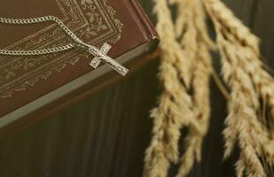 collar de plata con cruz crucifijo en el libro de la santa biblia cristiana sobre una mesa de madera negra. pidiendo bendiciones de dios con el poder de la santidad foto