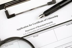 N-600 Application for Certificate of Citizenship blank form on A4 tablet lies on office table with pen and magnifying glass photo