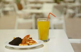 Glass of orange juice with plastic straw on white table in restaurant outdoor lounge zone photo