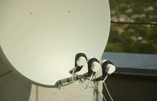 White satellite dish with three converters mounted on residental building rooftop concrete wall. Satellite television photo