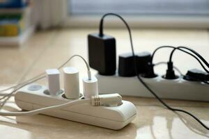 Overloaded power boards. Power strips with different electrical plugs on white floor photo