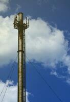 High metal chimney of industrial plant with ladder in the form of metal braces against the background of a cloudy blue sky photo