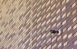 Black wireless CCTV security camera for area surveillance placed on brick wall. Surveillance cameras are modern technology to prevent thieves photo