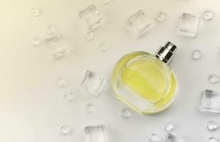 frasco amarillo de perfume femenino, fotografía objetiva del frasco de perfume en cubitos de hielo y agua sobre una mesa blanca. vista desde arriba. foto de producto de maqueta, concepto de frescura