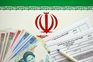 Iranian annual income tax return form F20-25-006 ready to fill on table with pen and iranian money on flag photo