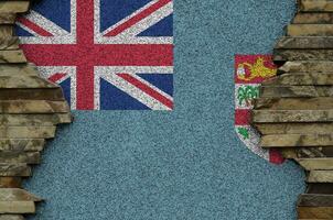 Fiji flag depicted in paint colors on old stone wall closeup. Textured banner on rock wall background photo