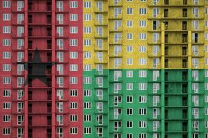 Guinea Bissau flag depicted in paint colors on multi-storey residental building under construction. Textured banner on brick wall background photo