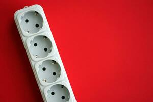 White electrical multi plug extender with european socket on bright red background photo