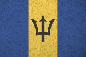 Barbados flag depicted in bright paint colors on old relief plastering wall. Textured banner on rough background photo
