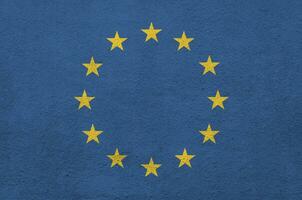 European union flag depicted in bright paint colors on old relief plastering wall. Textured banner on rough background photo