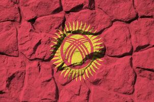 Kyrgyzstan flag depicted in paint colors on old stone wall closeup. Textured banner on rock wall background photo