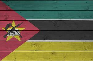 Mozambique flag depicted in bright paint colors on old wooden wall. Textured banner on rough background photo
