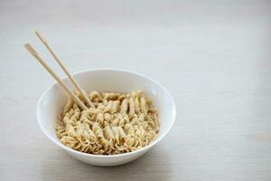 Bowl of instant cooking noodles with wooden chopsticks on white wooden table photo