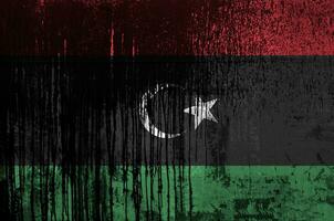 Libya flag depicted in paint colors on old and dirty oil barrel wall closeup. Textured banner on rough background photo