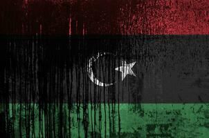 Libya flag depicted in paint colors on old and dirty oil barrel wall closeup. Textured banner on rough background photo