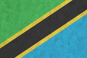 Tanzania flag depicted in bright paint colors on old relief plastering wall. Textured banner on rough background photo