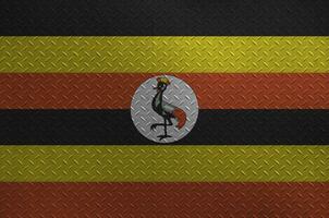 Uganda flag depicted in paint colors on old brushed metal plate or wall closeup. Textured banner on rough background photo
