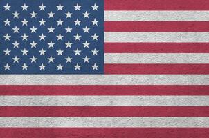 United States of America flag depicted in bright paint colors on old relief plastering wall. Textured banner on rough background photo