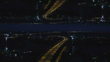 aéreo noche ver de un río puente con Moviente carros y el ciudad con noche luces, espejo horizonte efecto. medios de comunicación. maravilloso paisaje de noche ciudad y el puente a través de el río, comienzo tema. foto