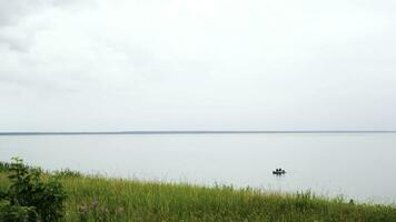 Green field and a calm lake with floating rubber boat. Concept. Fresh green grass and flowers on the shore of the big lake on cloudy sky background in the summertime. photo