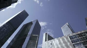 Bottom view of tops of glass skyscrapers on background blue sky. Action. Modern architecture of business centers reflecting blue sky. Dizzying view of modern glass skyscrapers photo