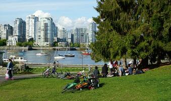 People enjoying a sunny spring day near the water in the park, with a stunning cityscape in the background. Vancouver, BC, Canada. May 02, 2021. photo