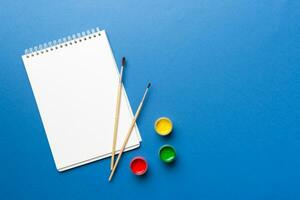 Album pages and paints, pencils, brush on a colored background. Top view with empty space. workplace for creativity. home teaching concept drawing photo