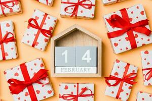 vista superior de cajas de regalo blancas con corazones y calendario de madera sobre fondo colorido. catorce de febrero. concepto del día de san valentín foto