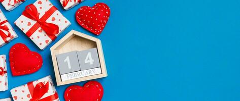 Holiday composition of gift boxes, wooden calendar and red textile hearts on colorful background with empty space for your design. The fourteenth of February. Top view of Valentine's Day concept photo