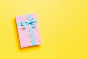 Gift box with blue bow for Christmas or New Year day on yellow background, top view with copy space photo