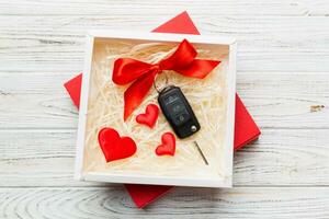 Black car key in a present box with a ribbon and red heart on colored background. Valentine day composition Top view photo