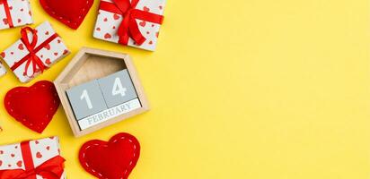 Top view of gift boxes, wooden calendar and red textile hearts on colorful background. The fourteenth of february. St Valentine's day concept with copy space photo