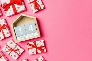 Holiday composition of gift boxes with red hearts and wooden calendar on colorful background with empty space for your design. The fourteenth of February. Top view of Valentine's Day concept photo