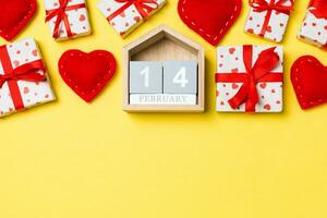 Holiday composition of gift boxes, wooden calendar and red textile hearts on colorful background with empty space for your design. The fourteenth of February. Top view of Valentine's Day concept photo