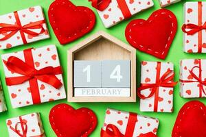 Top view of gift boxes, wooden calendar and red textile hearts on colorful background. The fourteenth of february. St Valentine's day concept with copy space photo