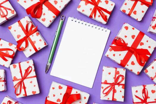 Holiday composition of notebook and gift boxes with red hearts on colorful background with empty space for your design. Top view of Valentine's Day concept photo