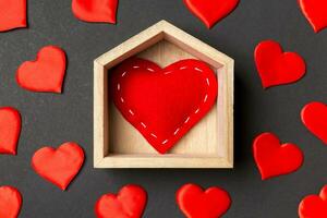 primer plano de corazón rojo en una casa de madera decorada con pequeños corazones sobre fondo colorido. día de San Valentín. concepto de hogar dulce hogar foto