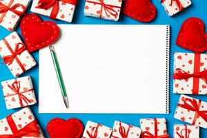 Top view of notebook surrounded with gift boxes and hearts on colorful background. Valentine's Day concept photo