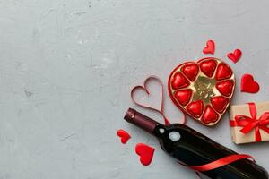 Bottle of red wine on colored background for Valentine Day with gift and chocolate. Heart shaped with gift box of chocolates top view with copy space photo