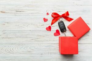 Black car key in a present box with a ribbon and red heart on colored background. Valentine day composition Top view photo