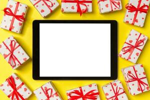 Top view of digital tablet surrounded with gift boxes on colorful background. Saint Valentine's day photo