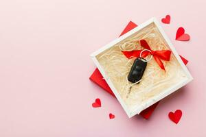 Black car key in a present box with a ribbon and red heart on colored background. Valentine day composition Top view photo