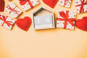 Top view of gift boxes, wooden calendar and red textile hearts on colorful background. The fourteenth of february. St Valentine's day concept with copy space photo