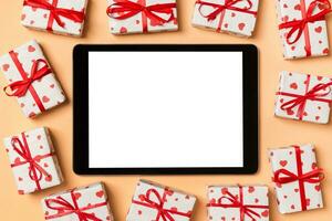 Top view of digital tablet surrounded with gift boxes on colorful background. Saint Valentine's day photo