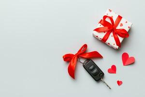 Black car key in a present box with a ribbon and red heart on colored background. Valentine day composition Top view photo